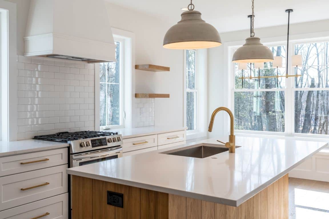 Half-circle pendants hang above a large kitchen island in a newly redesigned kitchen decorated in whites and natural oaks.