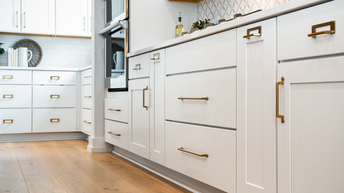 Freshly painted white shaker kitchen cabinets with brass hardware and a hardwood floor