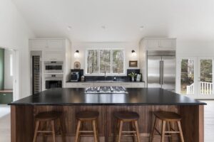 Walnut kitchen island with honed black countertop and counter stools in a Yarmouth, Maine home